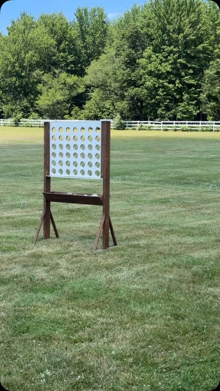 Giant wooden Connect Four game standing on a green lawn with trees behind.