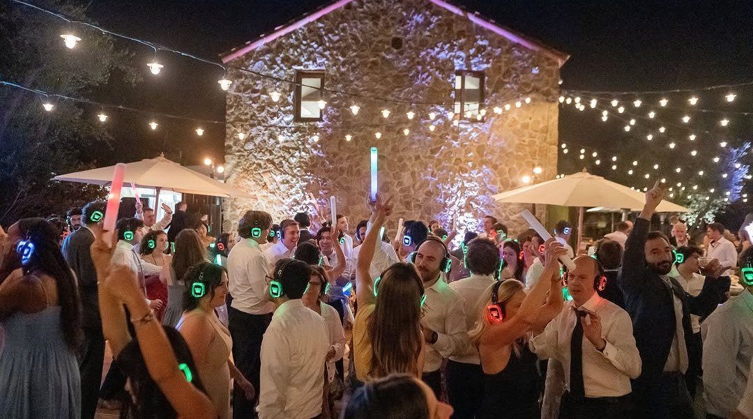 People dancing at night wearing glowing LED headphones for a silent disco party.