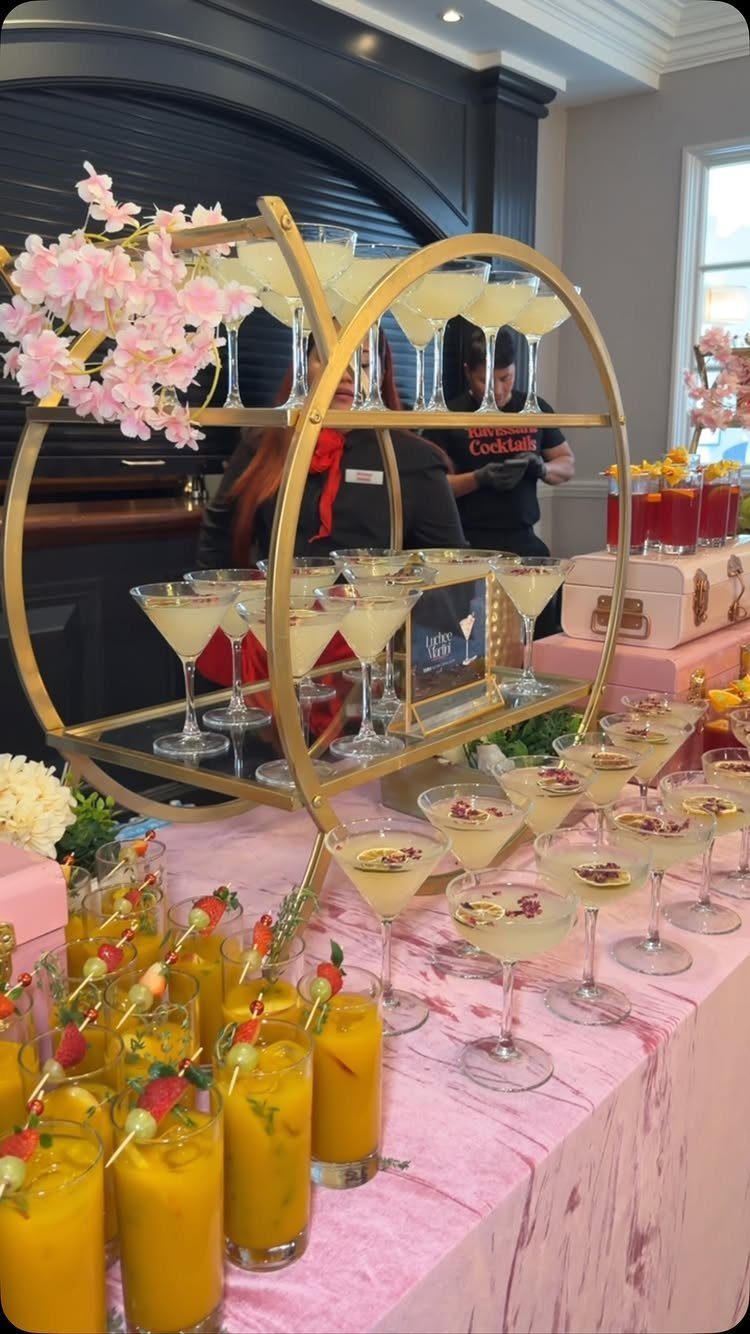 Gold tiered stand with yellow cocktails on a pink marble table with blossoms.