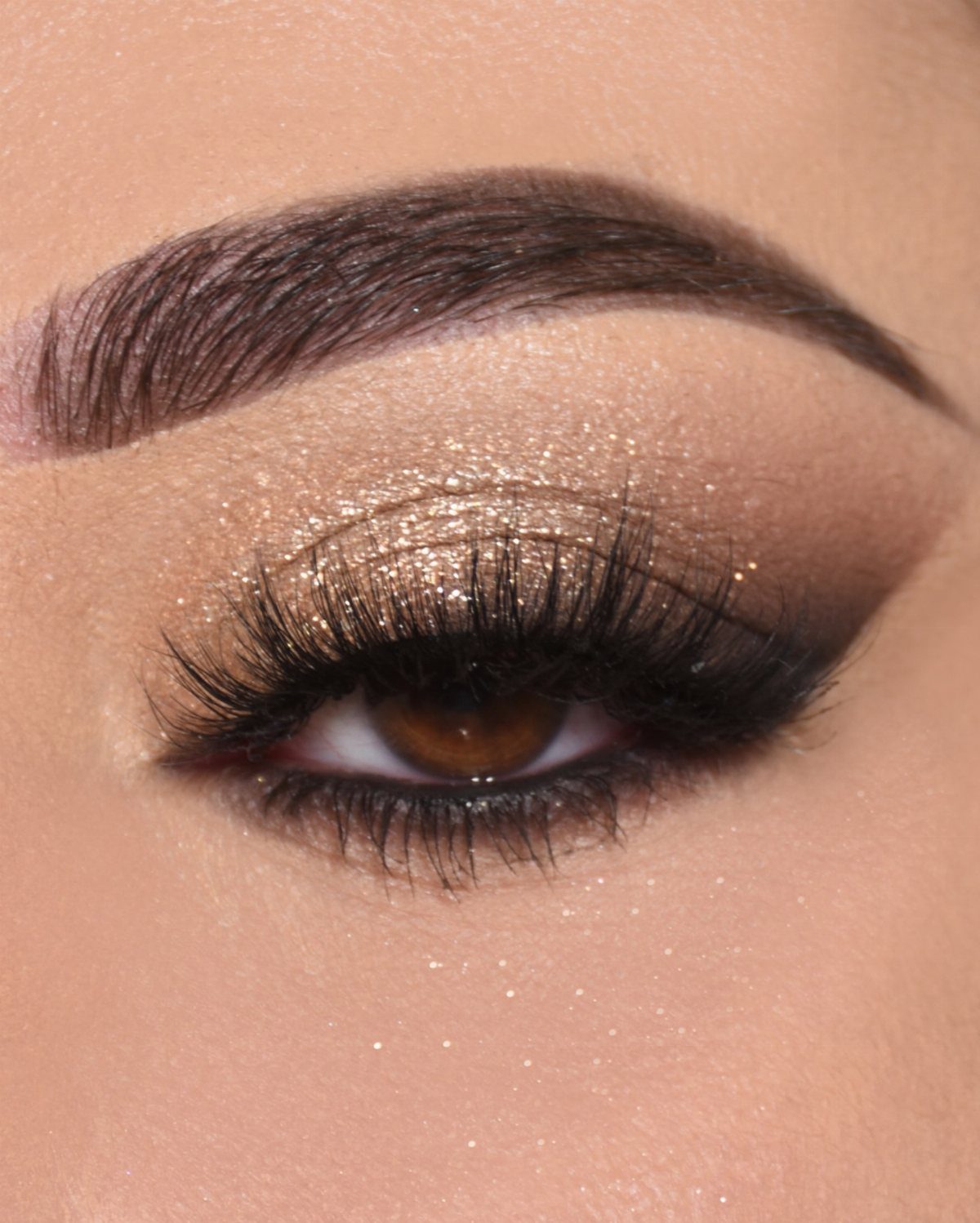 Eye with gold shimmering eyeshadow, dark brown blending, and long voluminous false lashes.