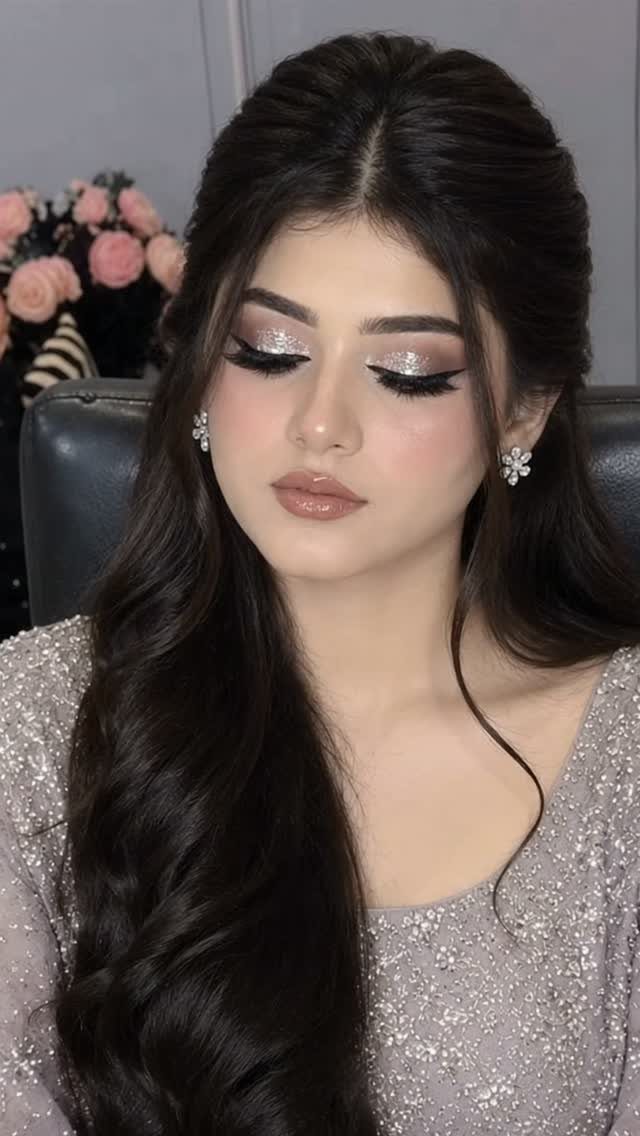 Woman with silver glitter eyeshadow, winged eyeliner, and long dark wavy hair.