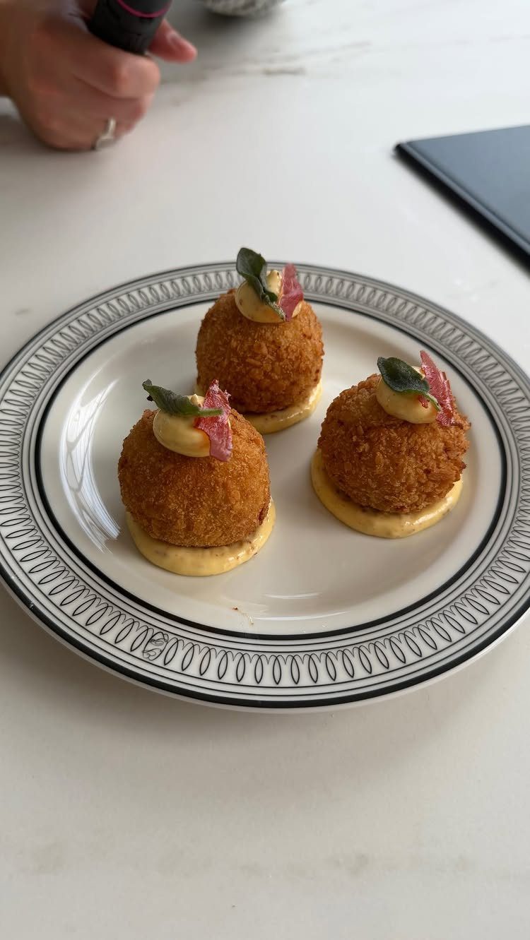 Three golden-brown arancini topped with cream and garnish on a decorative white plate.