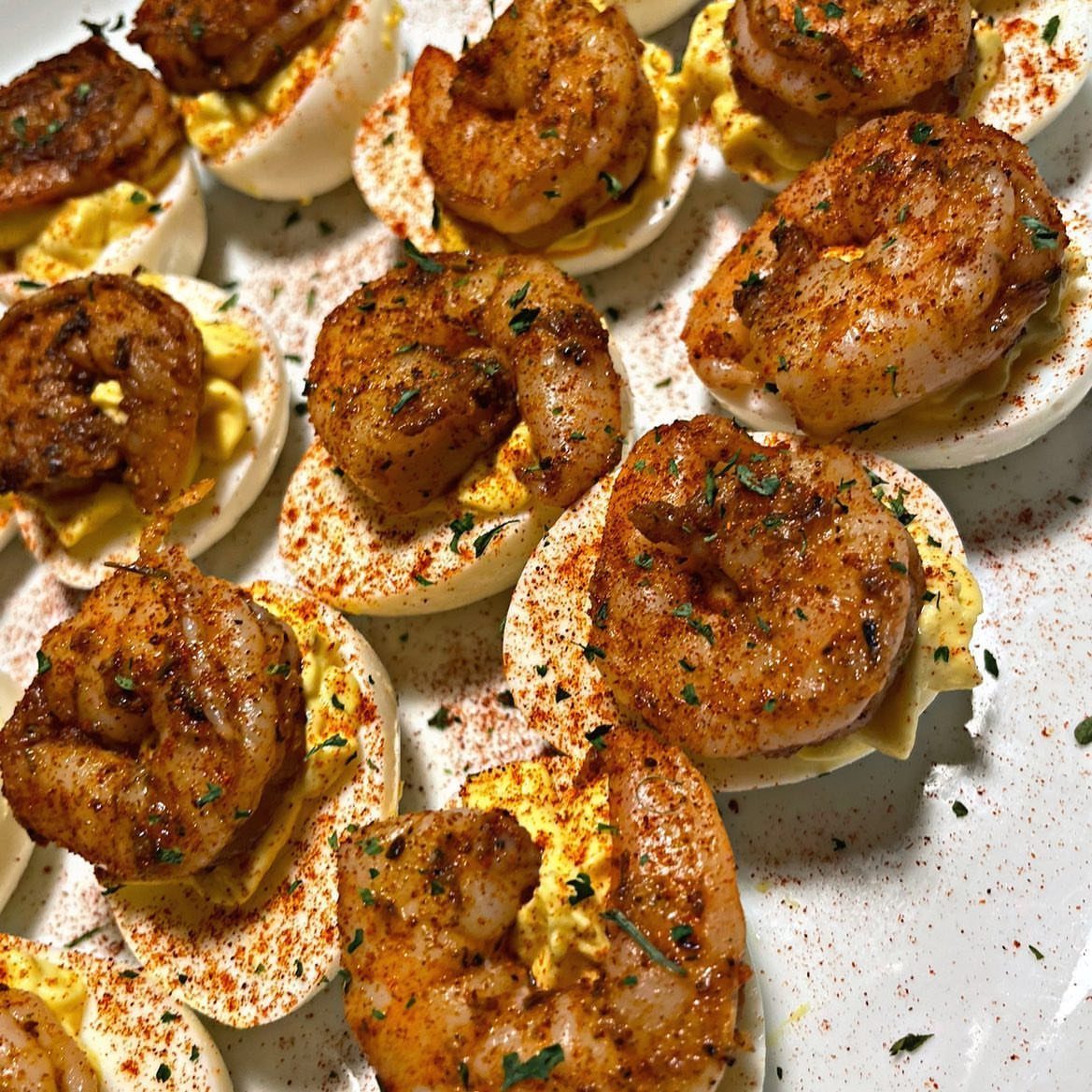 Deviled eggs topped with seasoned grilled shrimp on a white serving platter