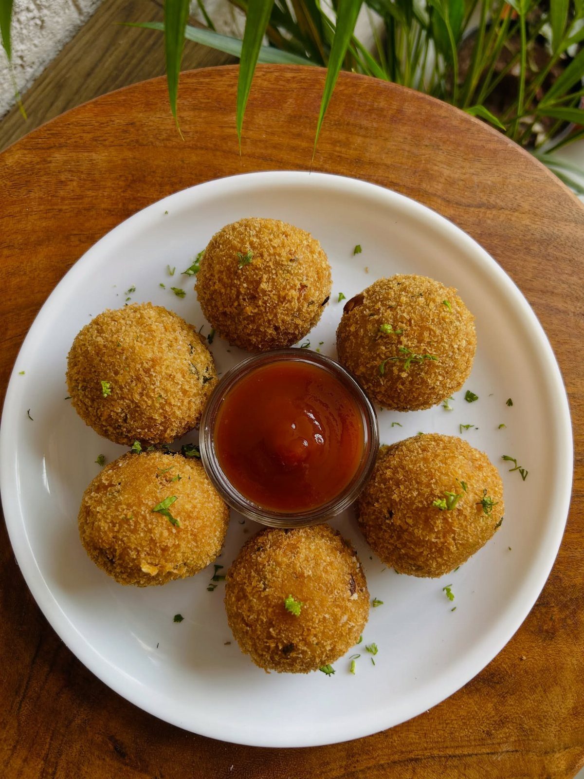 Fried breaded cheese balls on a white plate with red dipping sauce.