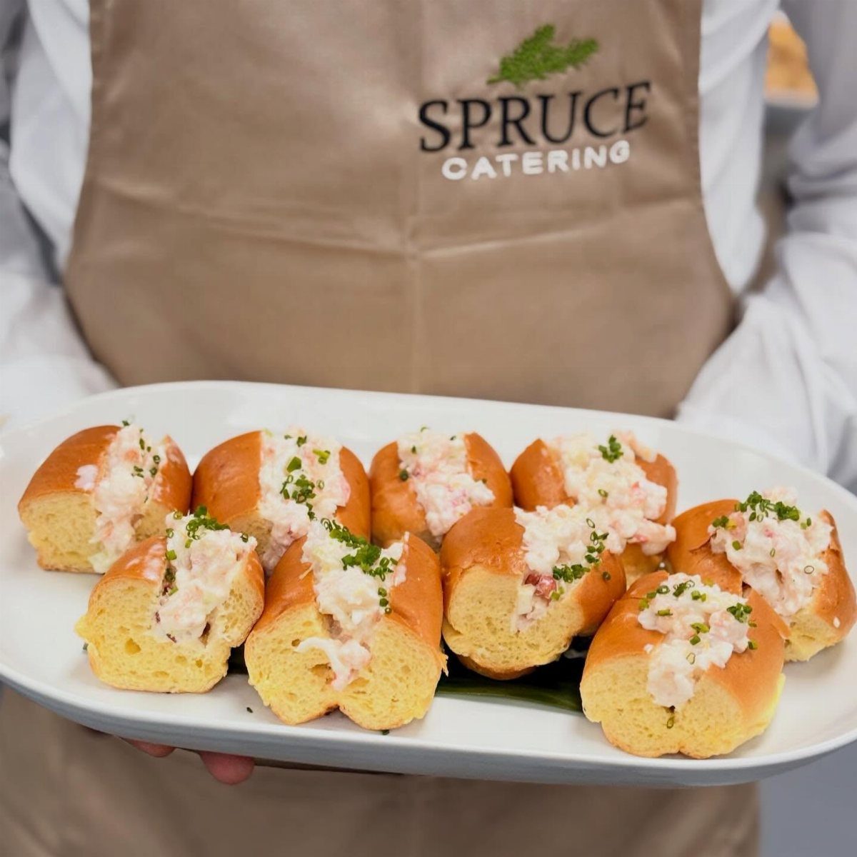 Mini lobster rolls on a white platter held by a catering professional.