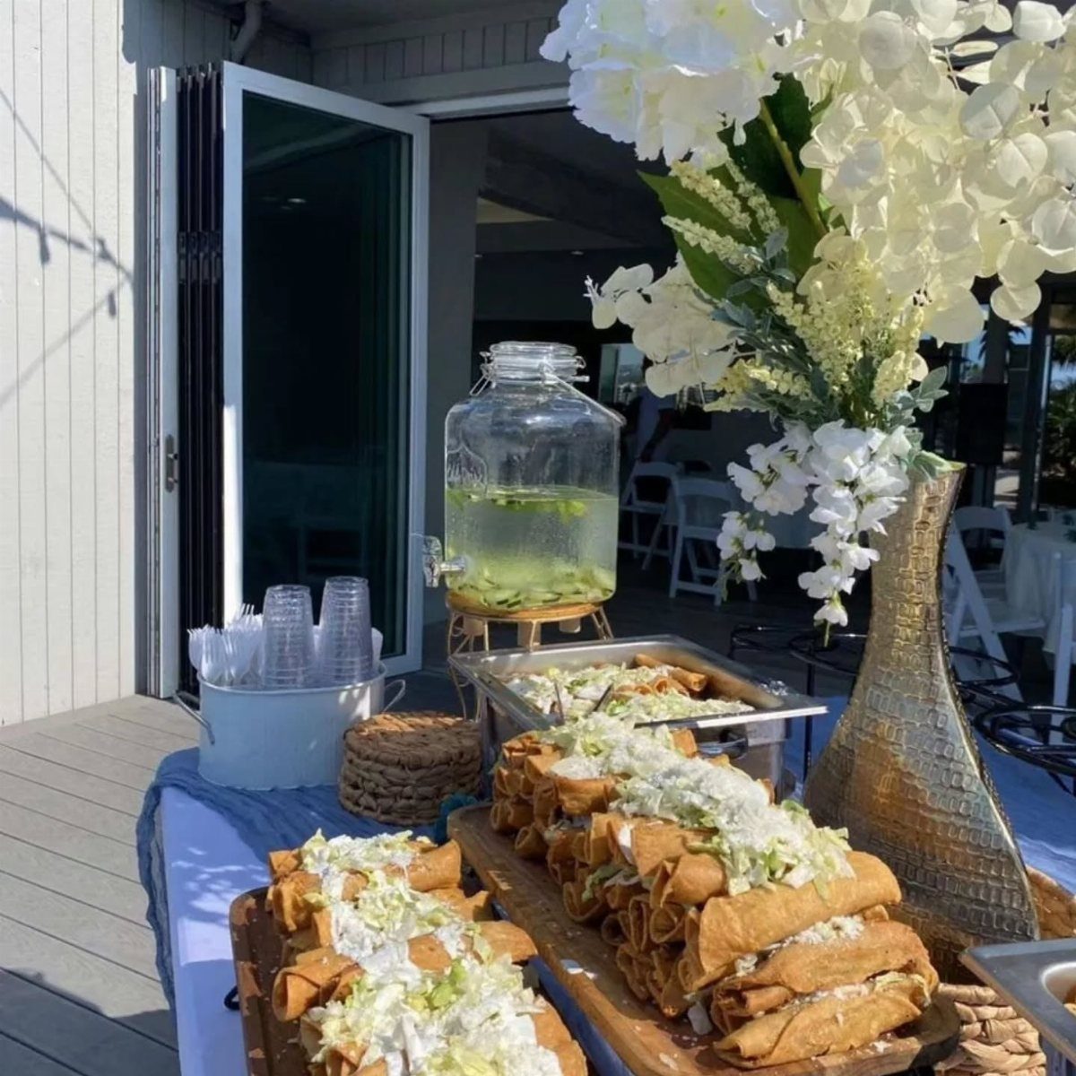 Small rolled tacos topped with lettuce and cream on a catering table.