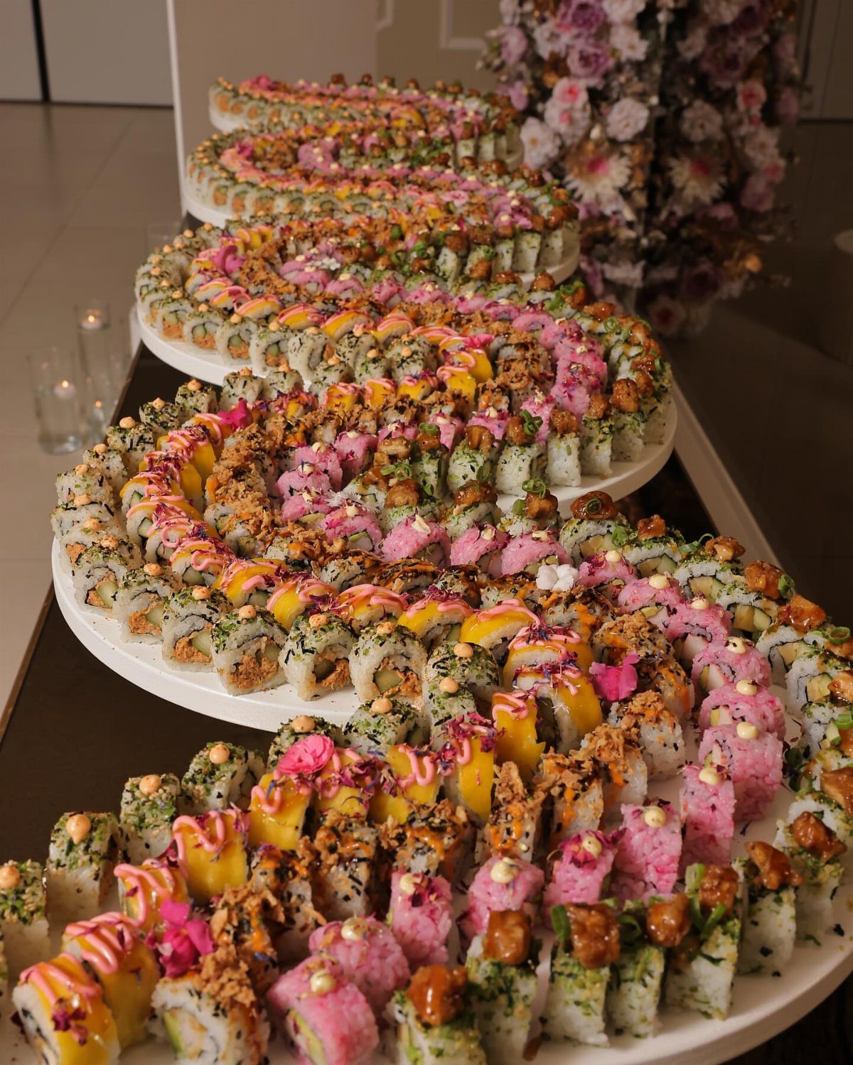 Colorful sushi rolls arranged in a winding serpentine pattern on white serving platters.