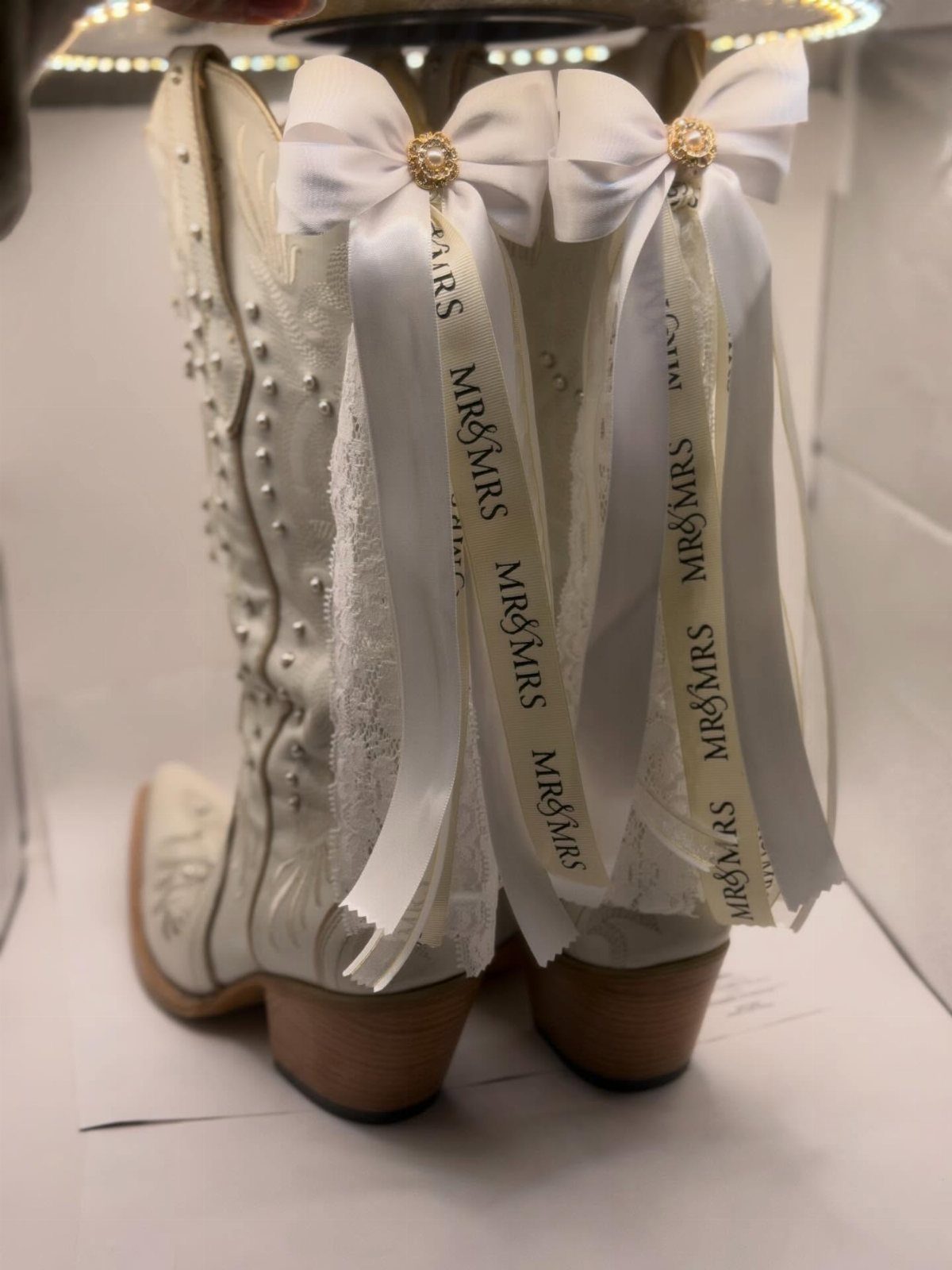 White cowboy boots decorated with white bows and Mr and Mrs ribbons.