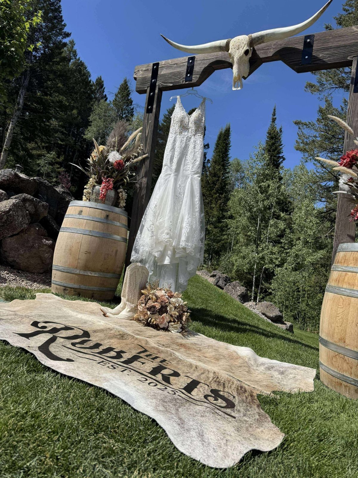 Personalized cowhide rug on grass with wedding dress and wooden arch outdoors