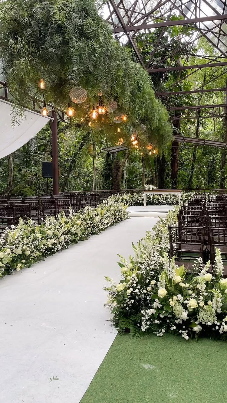 White floral arrangements lining a wedding aisle under a canopy of hanging greenery