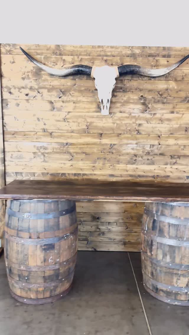 Rustic wooden table supported by barrels against a wood wall with steer skull