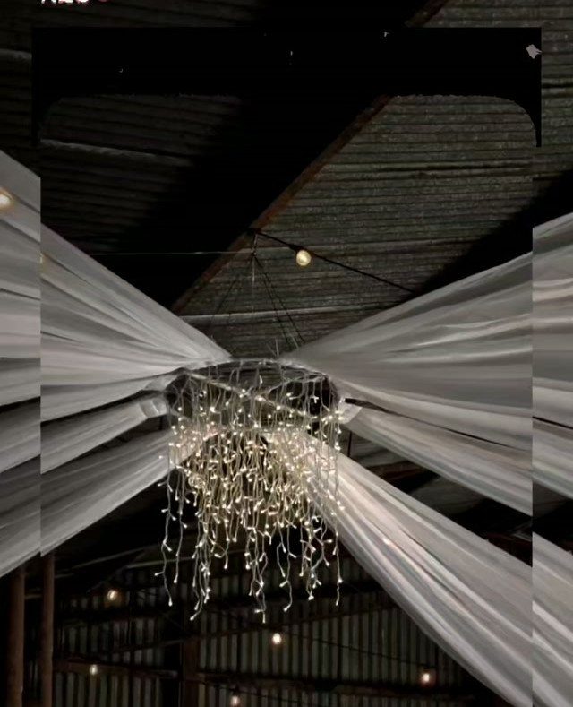White fabric draping and hanging fairy lights in a rustic barn ceiling
