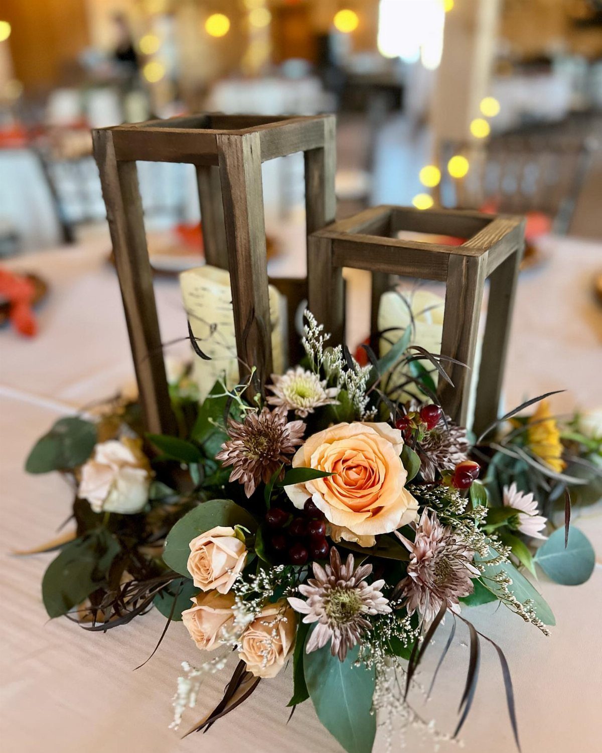 Wooden lanterns with white candles and peach roses on a wedding table