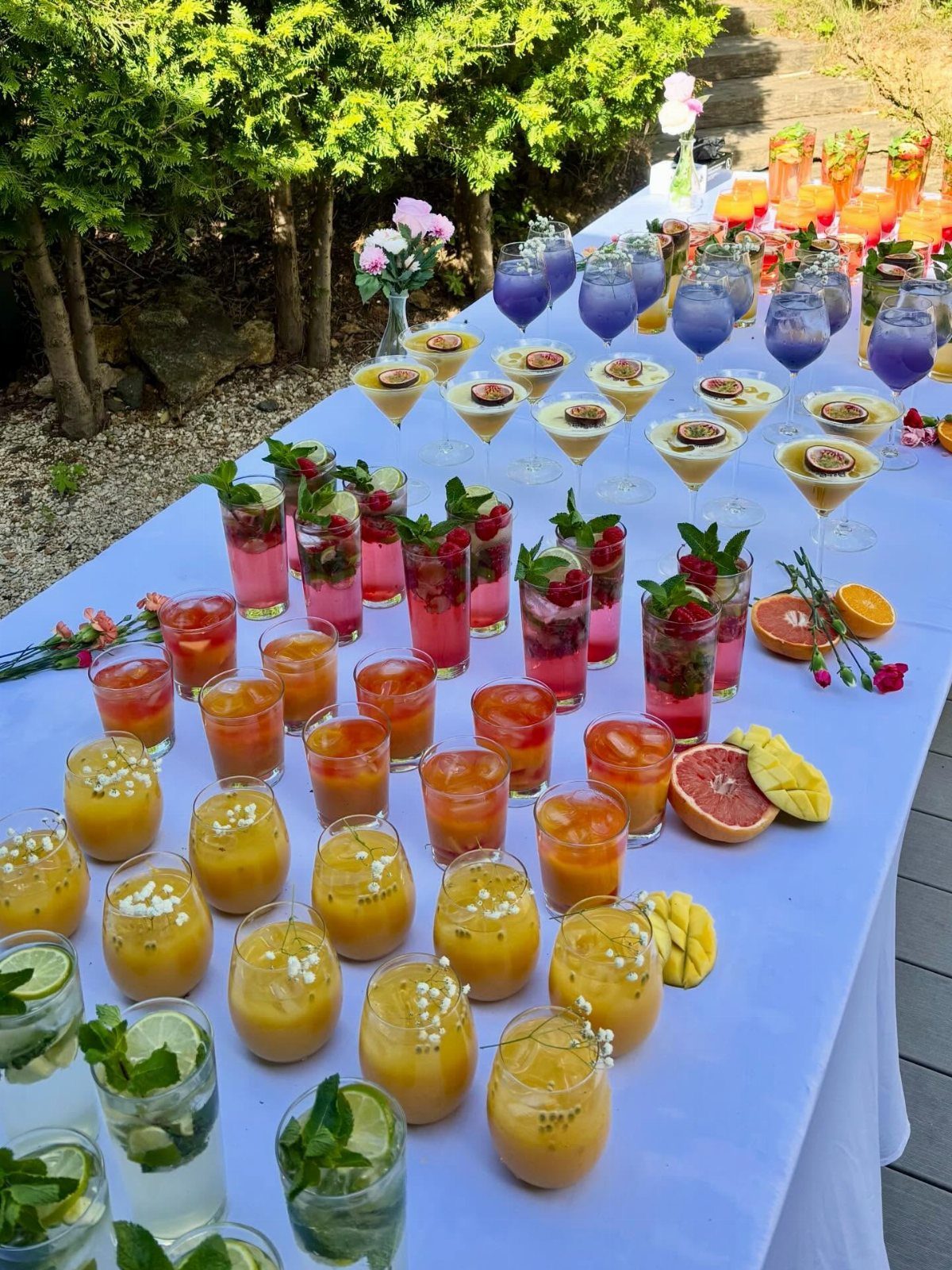 Colorful cocktails and mocktails with edible flower garnishes on a white outdoor table