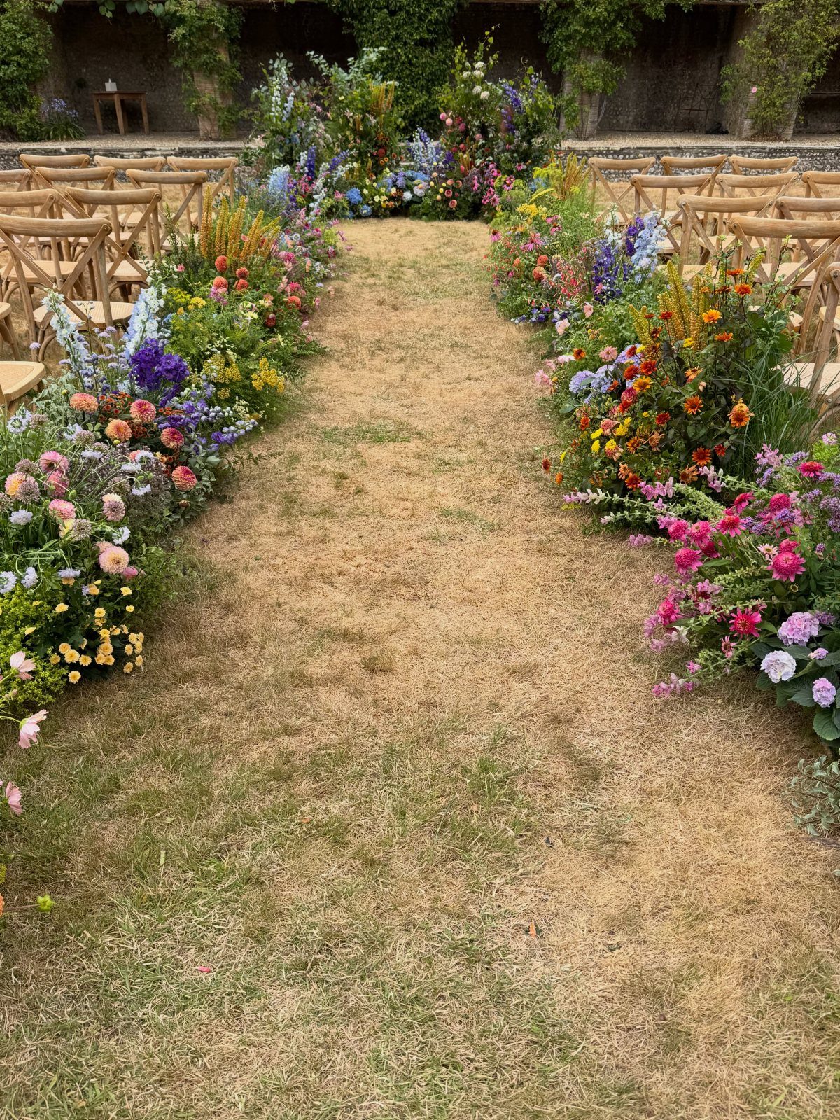Colorful flower arrangements lining a grassy wedding aisle with wooden chairs and altar.
