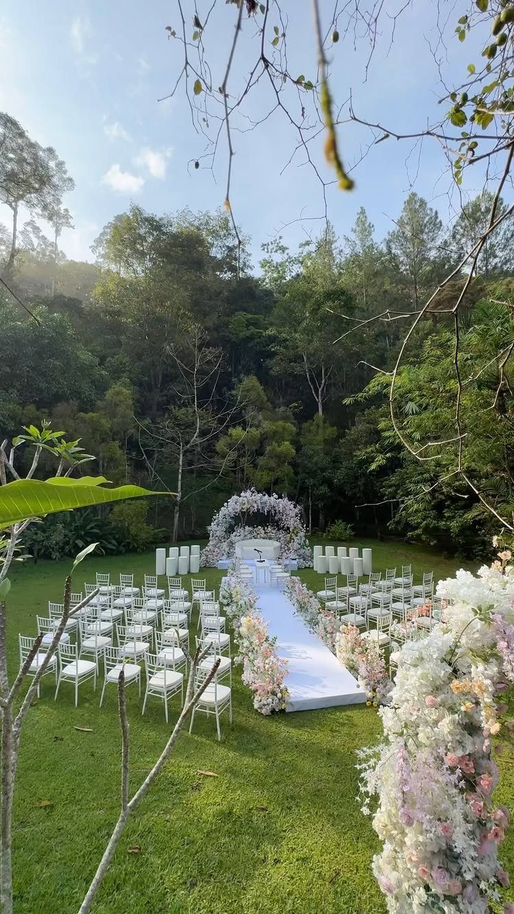 White floral ceremony arch at the end of a white aisle in a garden