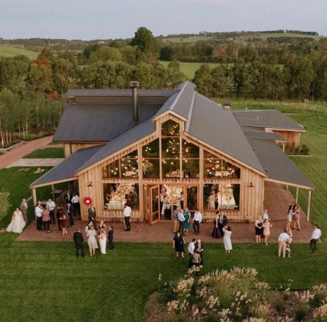Modern wooden wedding barn with glass walls and guests gathering on the lawn