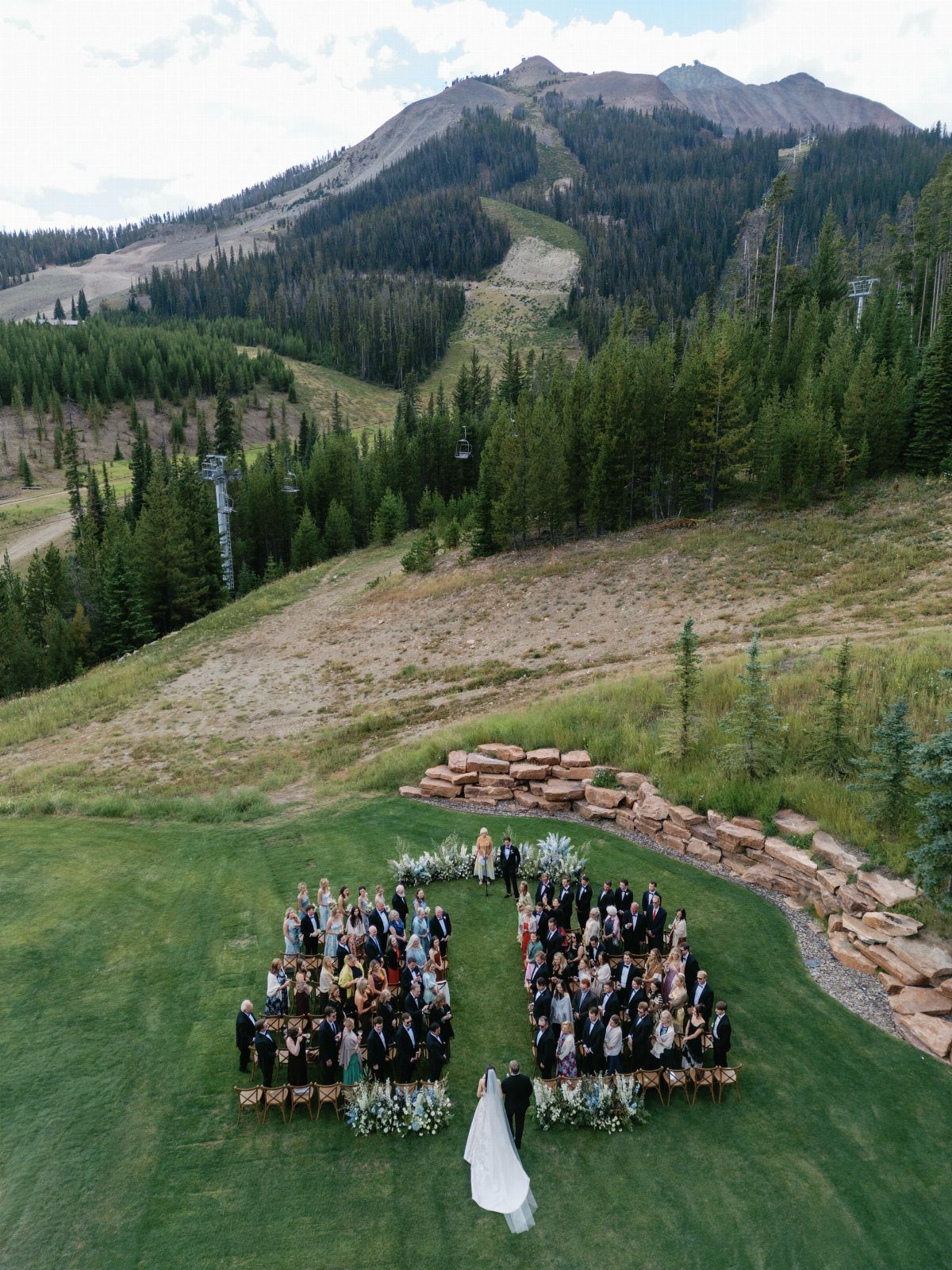 Wedding guests forming a heart shape on a lawn with mountain views behind.