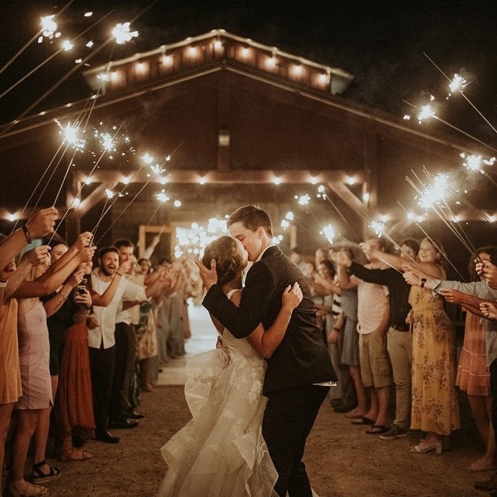 Bride and groom embracing at night surrounded by guests holding bright lit sparklers.