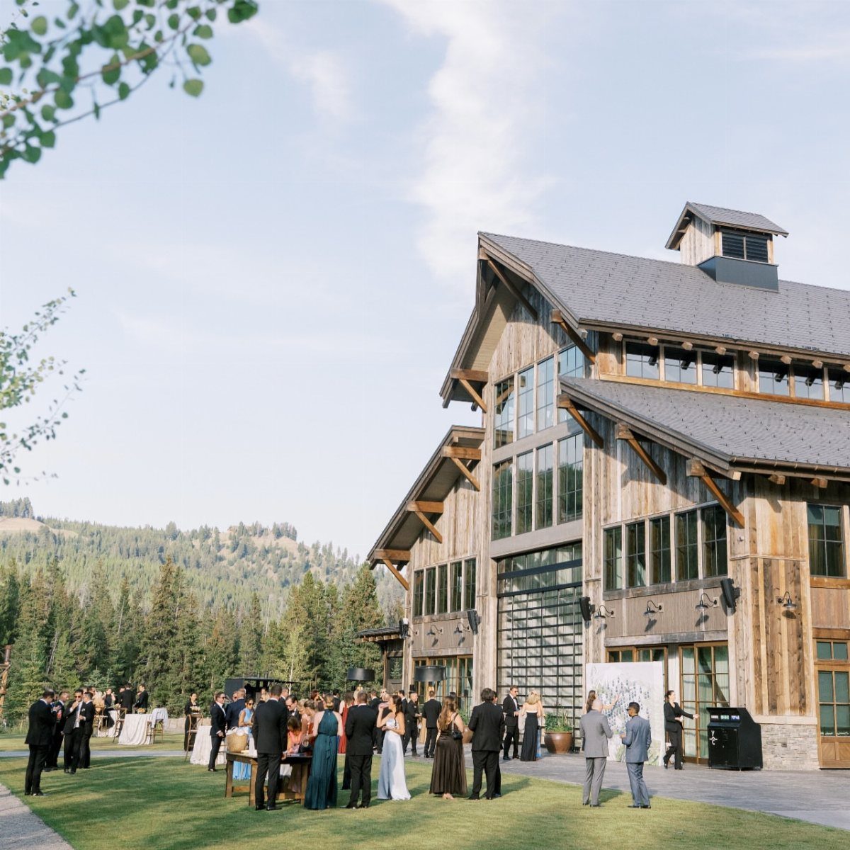 Formal wedding guests gathering outside a rustic wooden lodge with mountain views.
