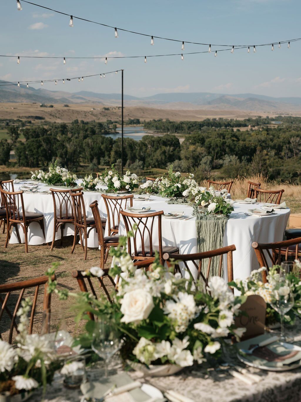 Wedding reception table with white flowers overlooking a mountain river valley in Montana