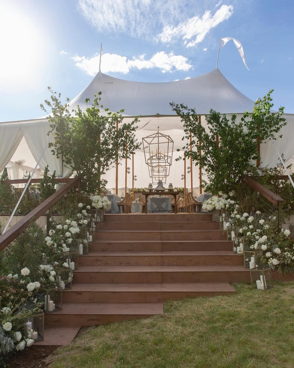 Wooden stairs with white floral arrangements leading to a white wedding tent.