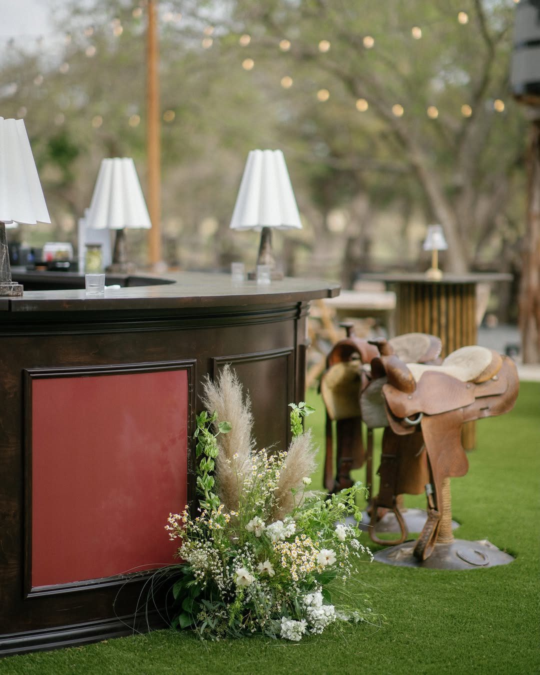 Outdoor event bar with white lamps, floral arrangements, and a western saddle
