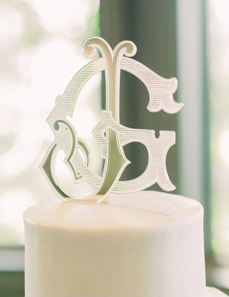 Silver monogram cake topper with intertwined letters on a white frosted cake