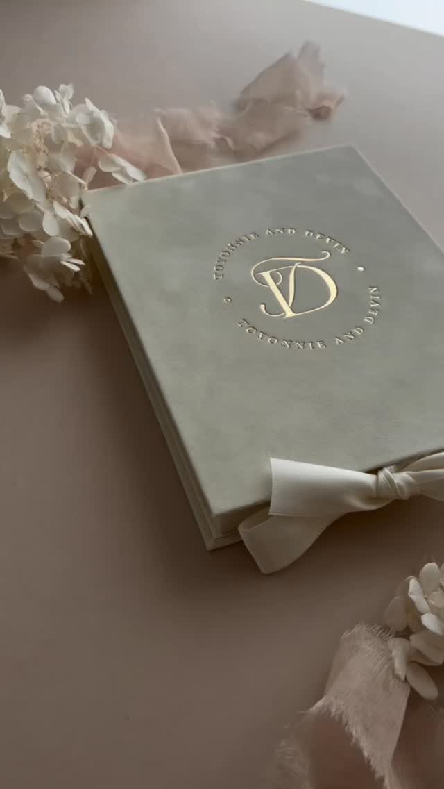 Grey wedding invitation with gold foil monogram tied with a white ribbon.