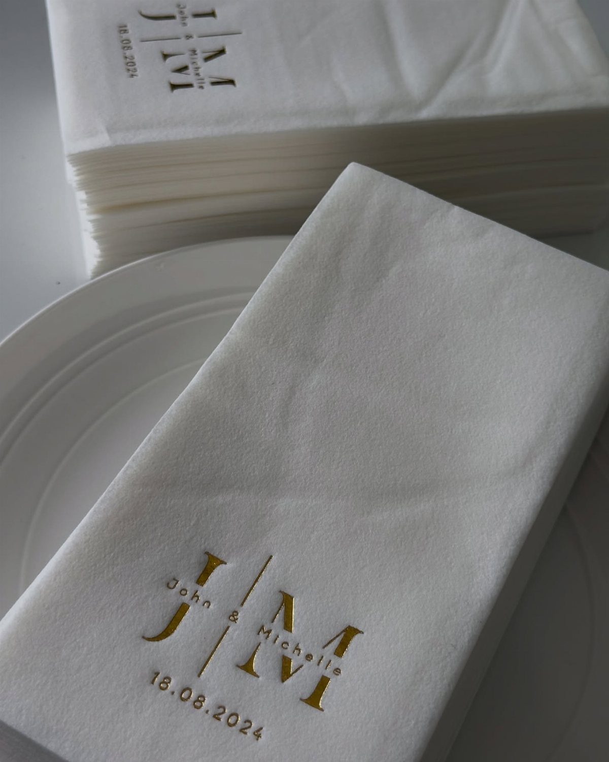 White paper napkins with a gold foil wedding monogram on a white plate