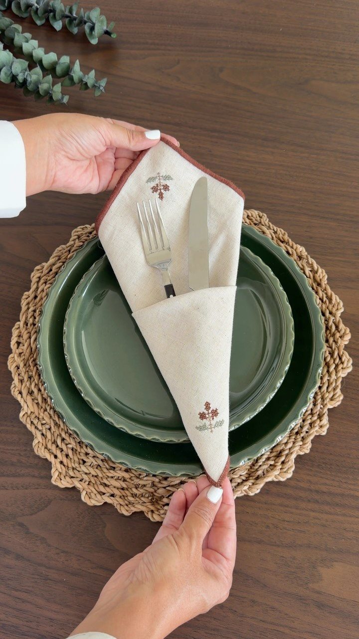Cream fabric napkin folded into a cone holding cutlery on green plates.