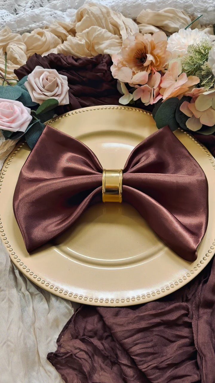 Brown satin napkin folded as a bow tie on a beige plate with roses.