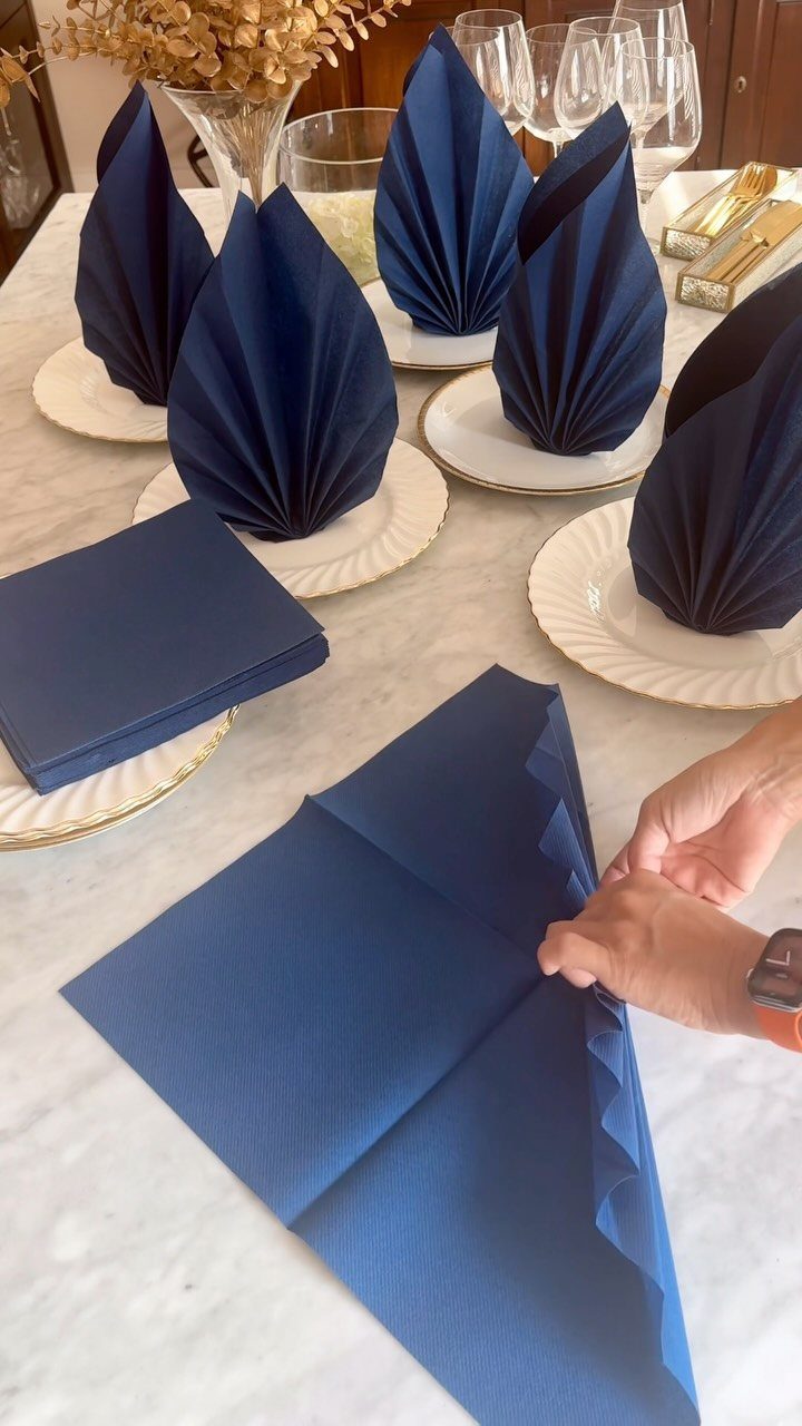 Navy blue napkins folded into fans standing on white plates on marble table