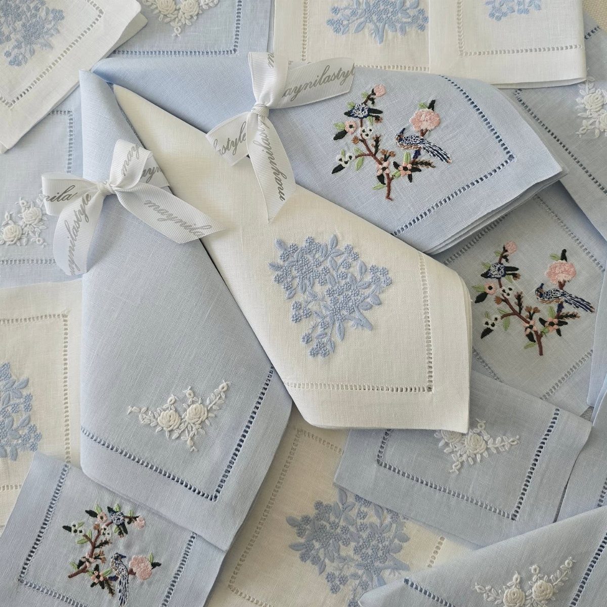 Light blue and white embroidered linen napkins with floral patterns and white ribbons.