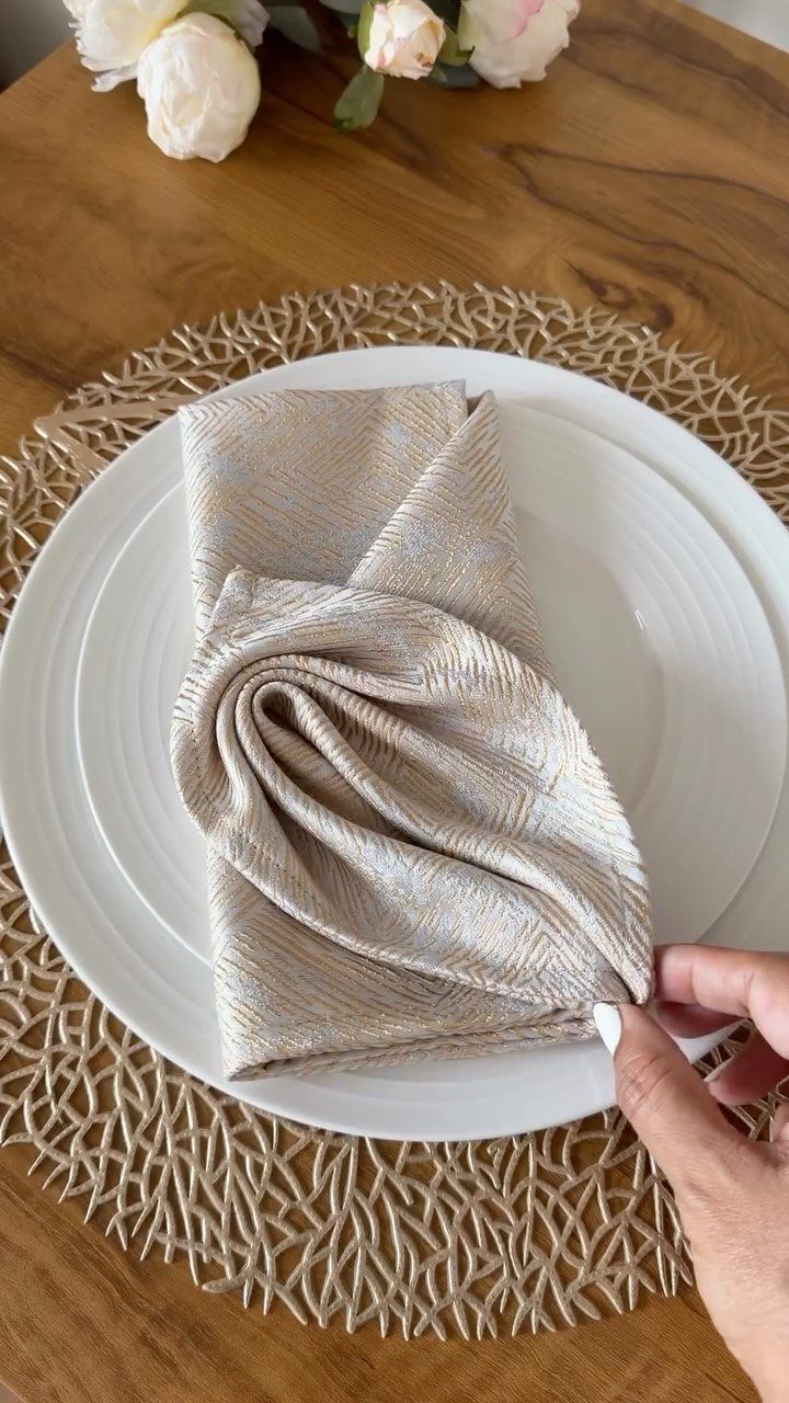 Beige textured fabric napkin folded on a white plate with gold placemat