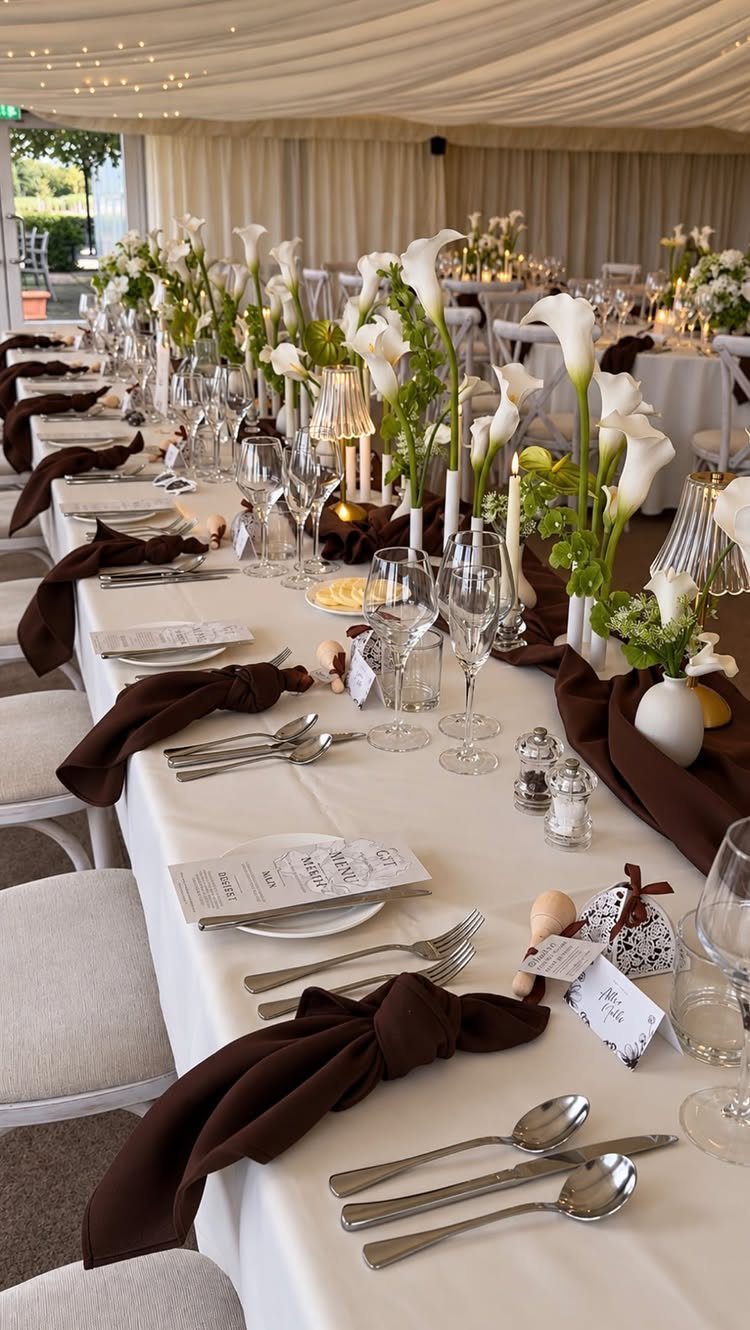 Brown knotted napkins on a white wedding table with white calla lily centerpieces.