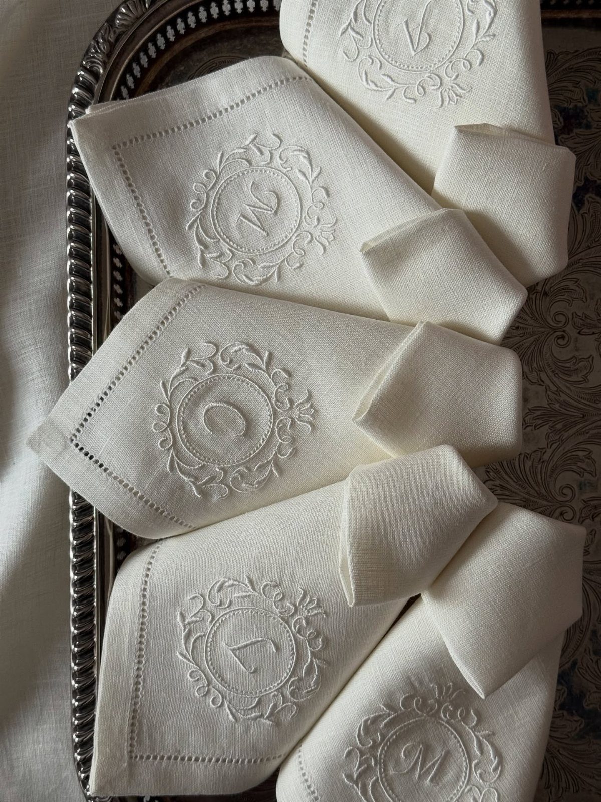 White linen-like napkins with embroidered monograms arranged on a silver decorative tray.