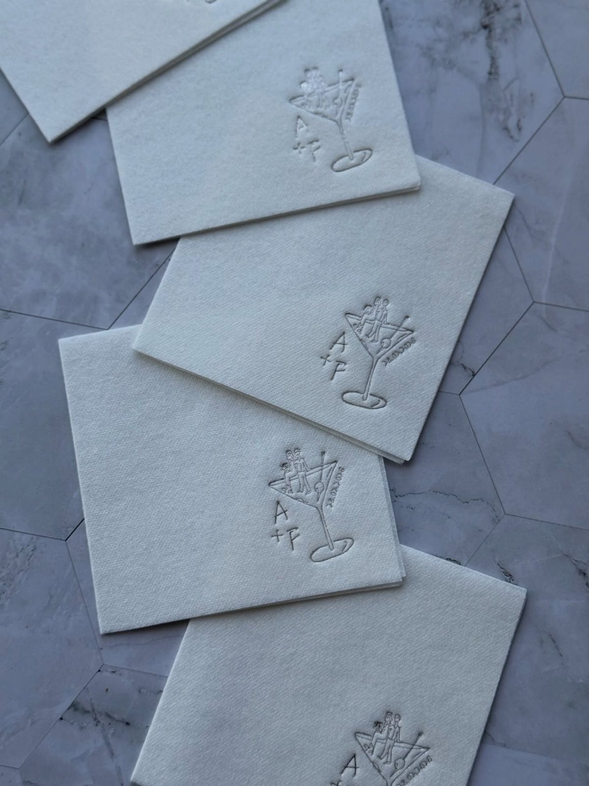 White square napkins with silver embossed cocktail glass and monogram on marble surface