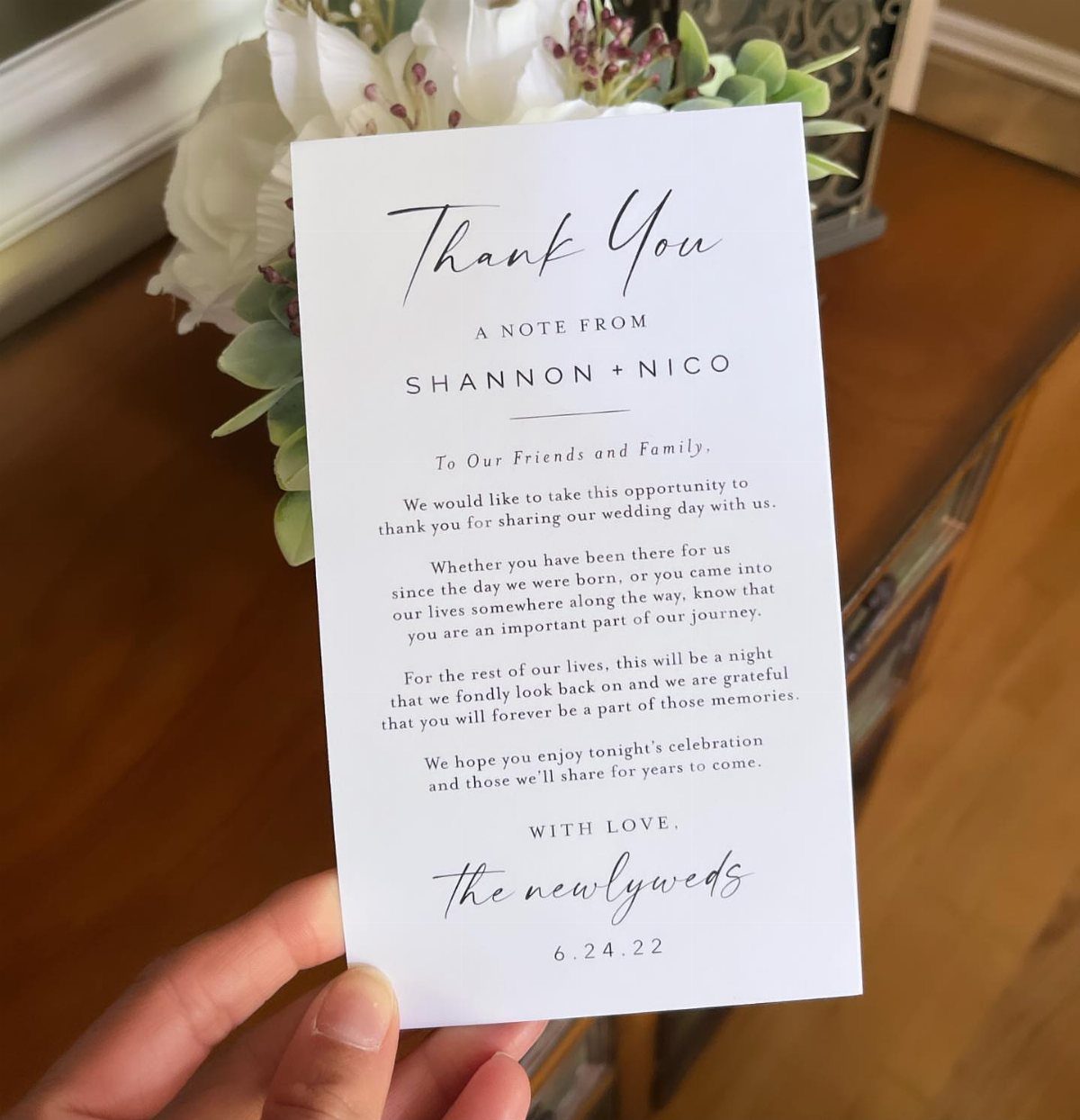 White thank you card with black script text held against white flowers.