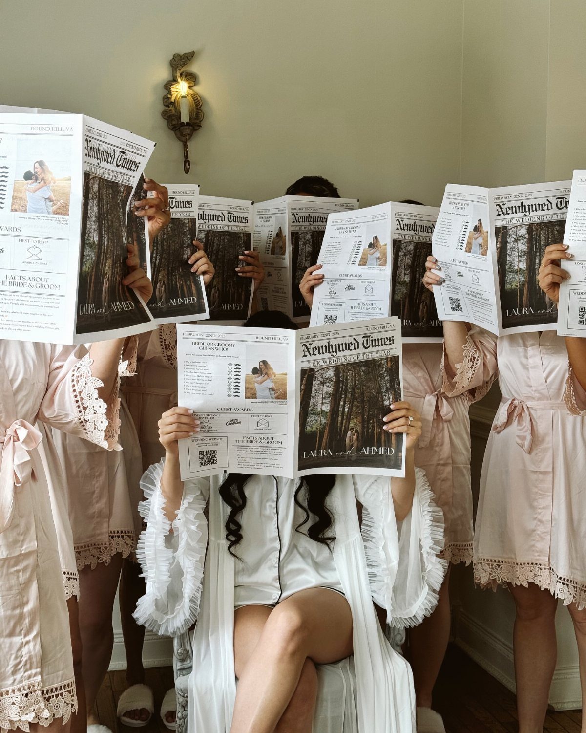 Women in satin robes holding wedding newspapers that cover their faces.