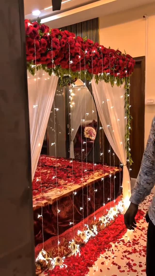 Bed decorated with red rose petals, white curtains, and twinkling fairy lights.