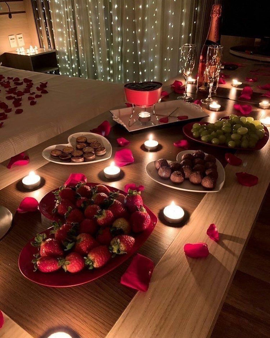 Romantic table setting with strawberries, chocolates, champagne, and candles with fairy light backdrop