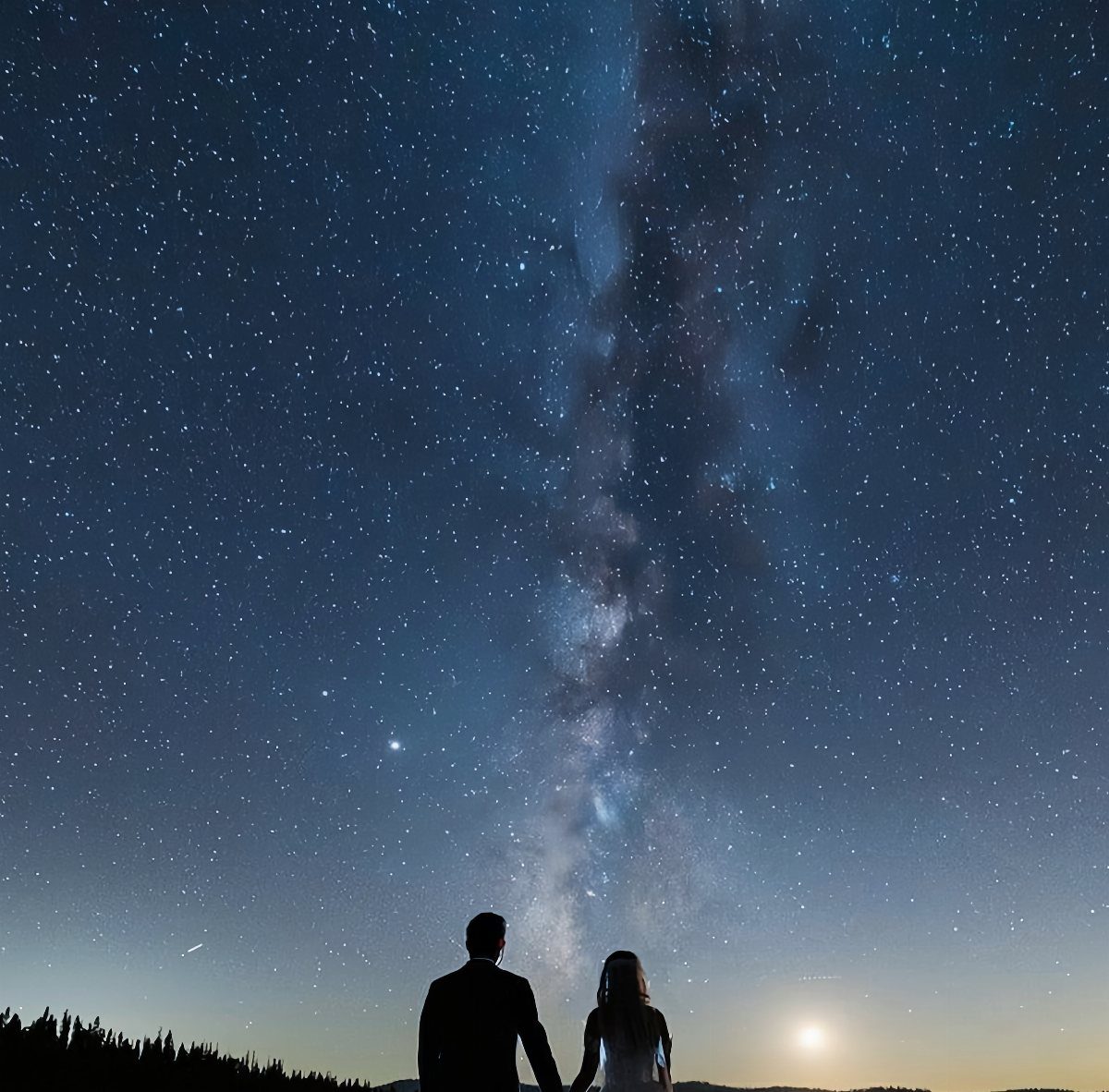 Silhouetted couple gazing at the Milky Way and stars in a night sky.