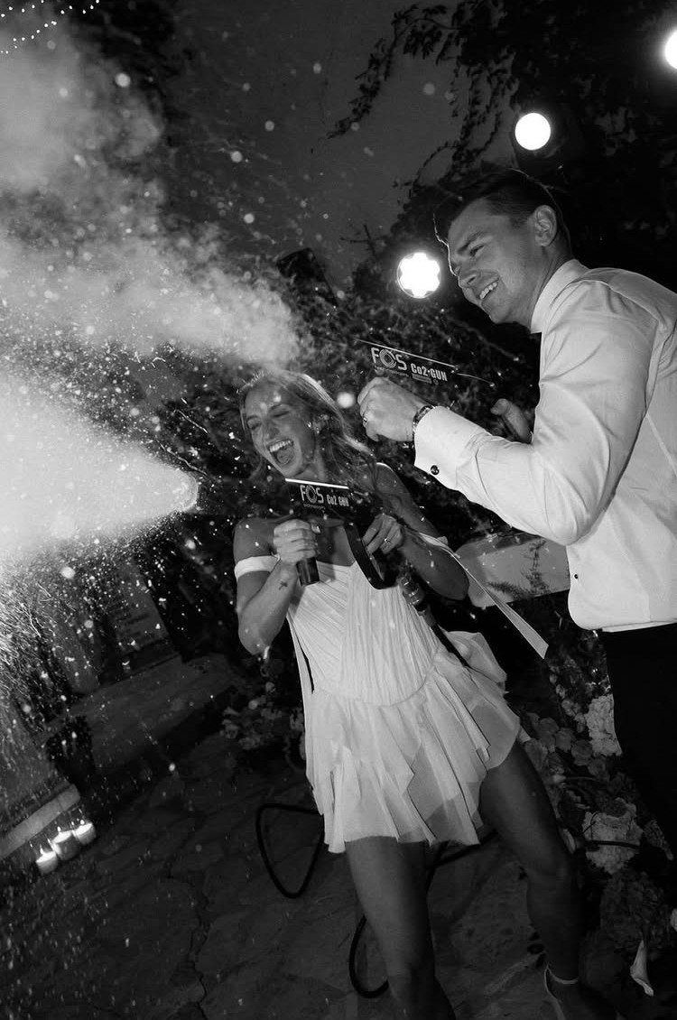Couple in white attire laughing while spraying water guns at night outdoors.