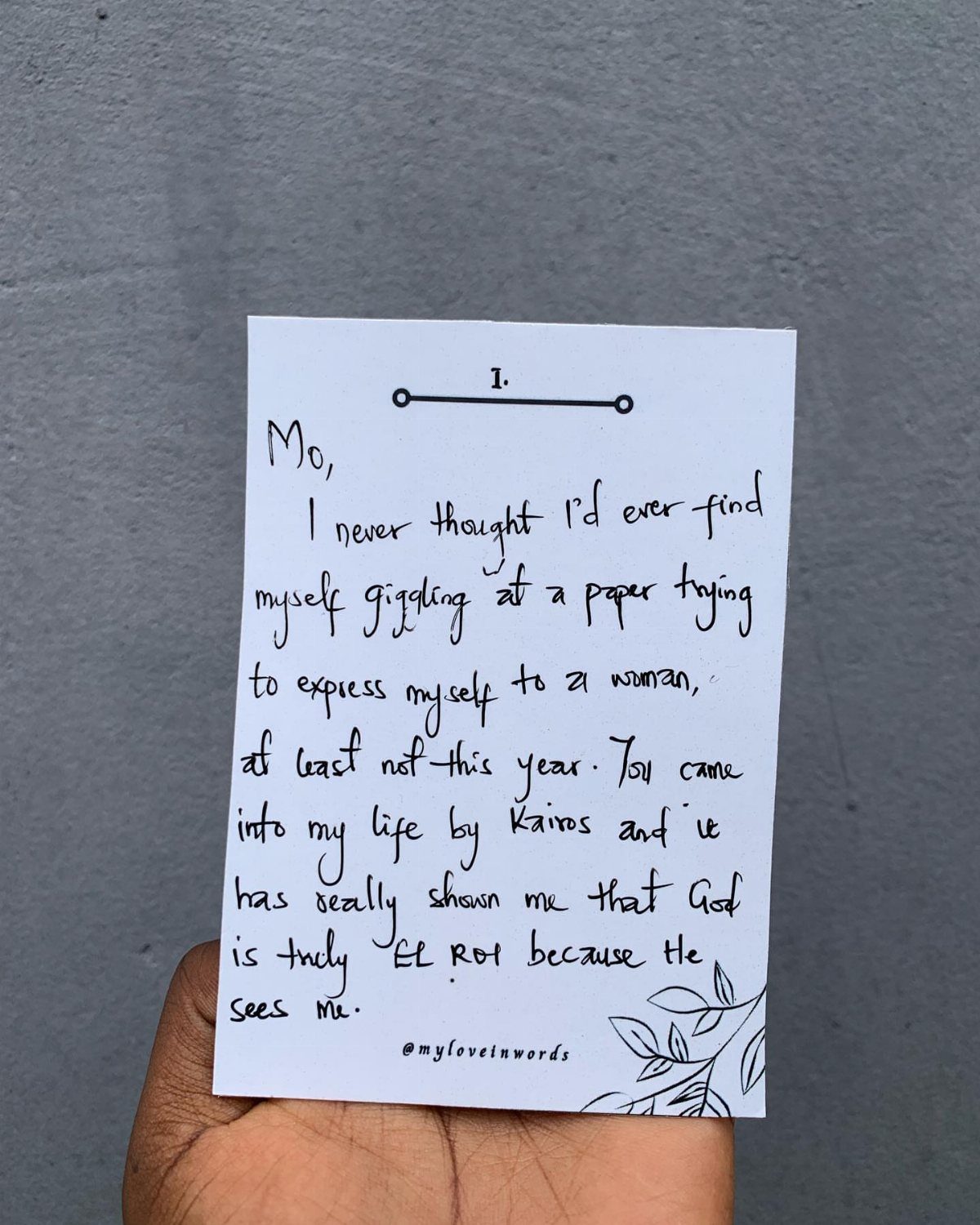 Hand holding a white card with a handwritten love note on a grey background