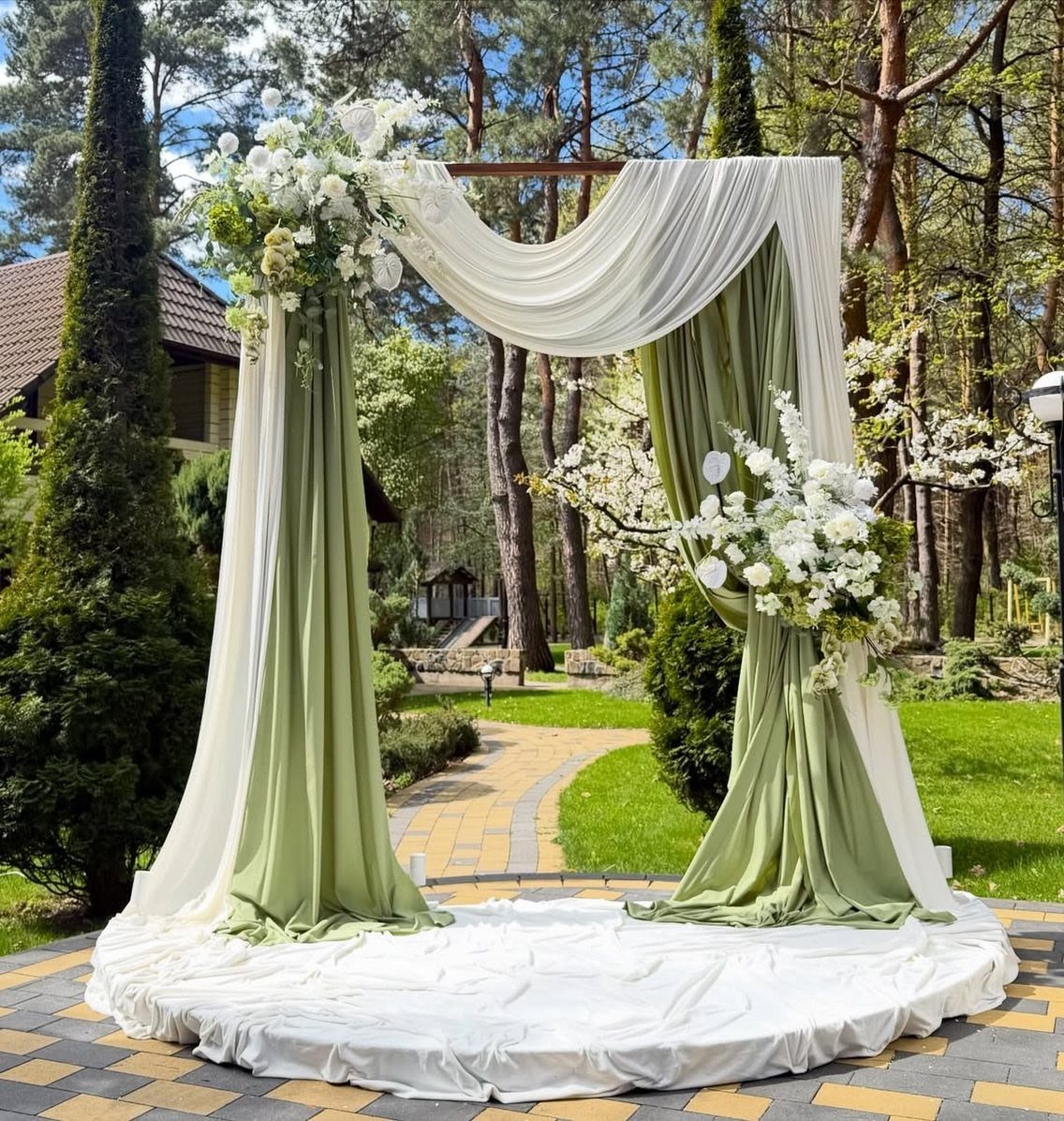 Wedding pergola draped in white and sage green chiffon with white floral arrangements