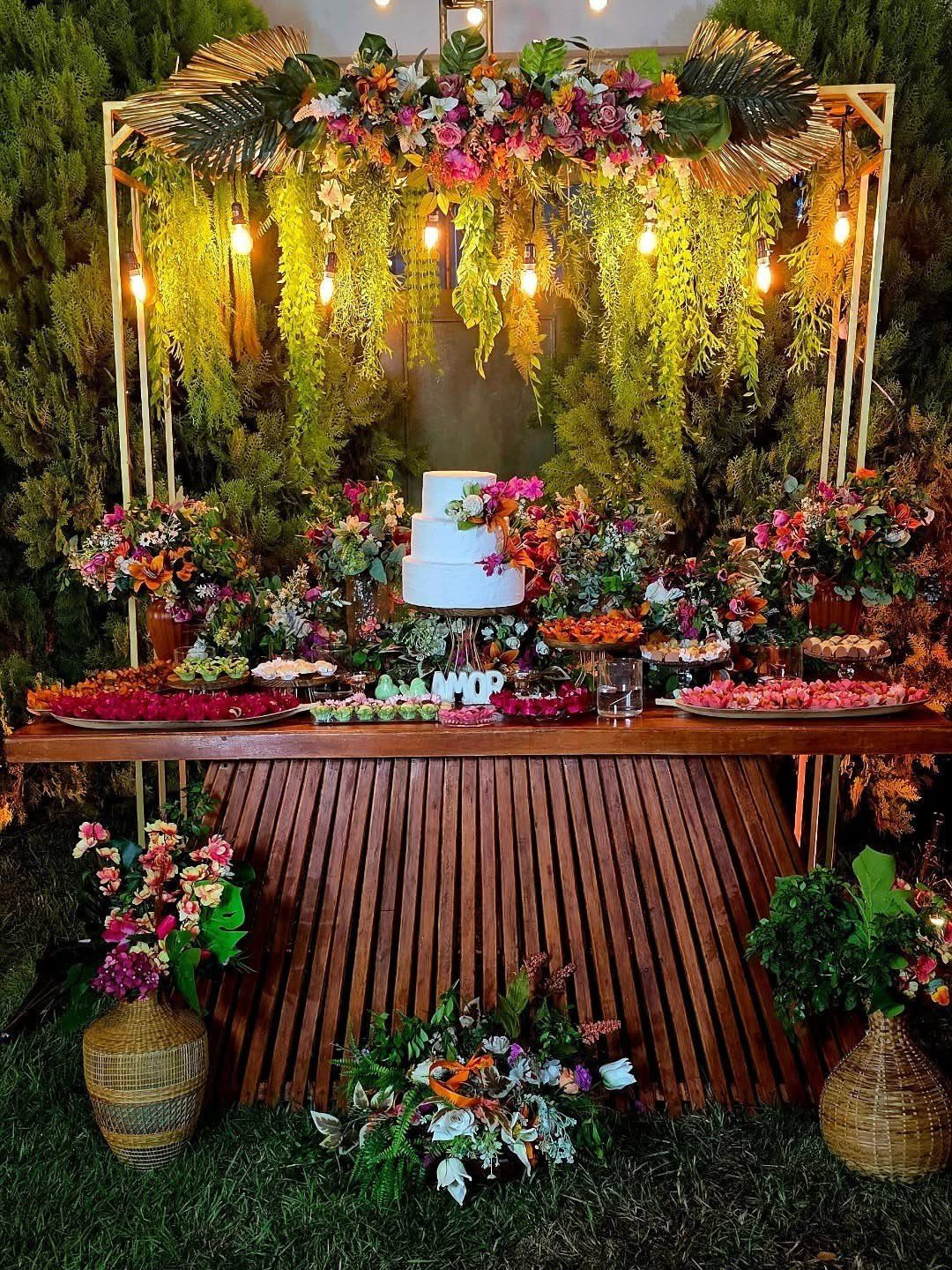 Dessert table with white cake and colorful flowers under a gold floral frame