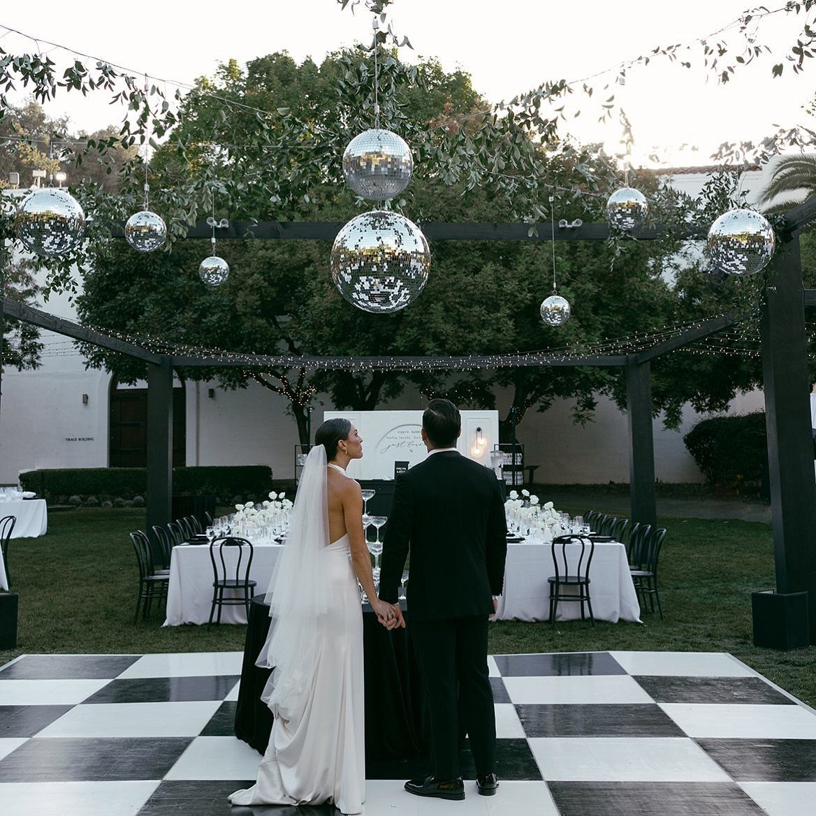 Bride and groom on checkered dance floor under pergola with hanging disco balls