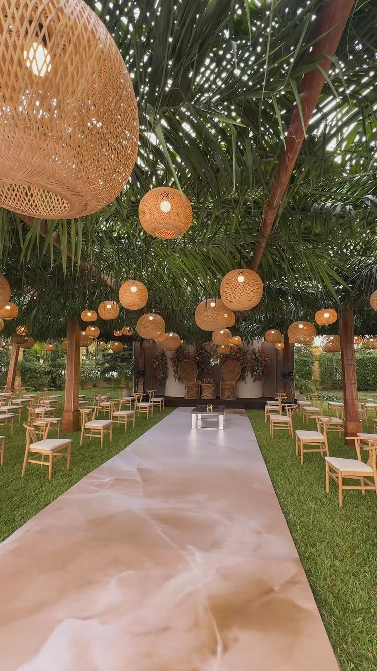 Wooden pergola with green foliage and rattan lanterns over a wedding ceremony aisle