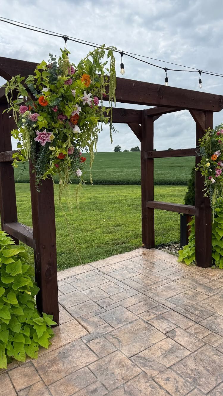 Wooden wedding pergola decorated with colorful flowers on a stamped concrete patio.